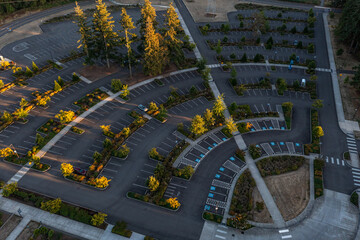 Aerial drone photo of an empty parking lot in Oregon City with landscaped rows, trees showing fall colors, and golden sunset light creating long shadows across the pavement and walkways