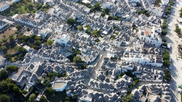 Aerial 4k footage of Alberobello in Apulia Italy, showing the famous trulli houses with their unique conical roofs, the historic town center, surrounding landscape, and clear blue skies on a sunny day