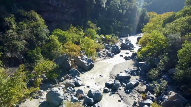 Aerial 4k drone footage of Gole Alcantara gorge in Sicily, Italy, showing the Alcantara river flowing through dramatic basalt rock formations, steep cliffs, and stunning natural landscape shaped by vo