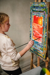 School kid drawing with brush landscapes on easel. Mix and combine colors. Child drew a picture in art class. Girl enjoys painting in a workshop. Art lesson. Education and learning concept.