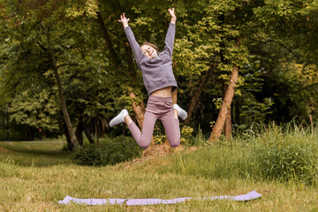 Excited child jumping with joy above yoga mat outdoors