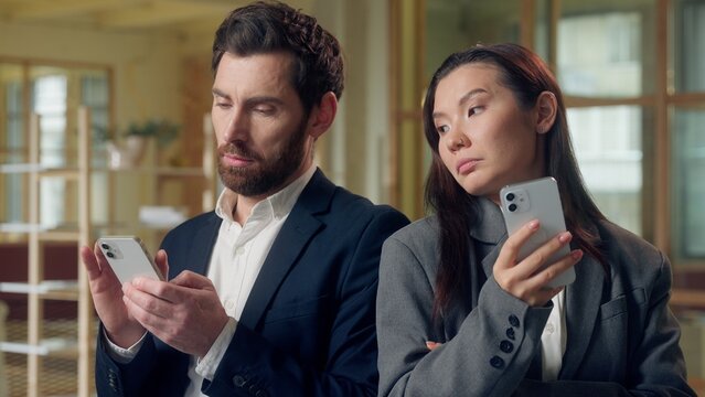 Multiethnic team Korean businesswoman glance at Caucasian businessman mobile phone expression business smartphone comparison play game success jealousy cellphone device office work application online