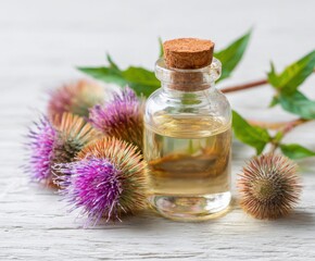 Burdock oil in a small glass bottle and burdock flowers on a white wooden table.