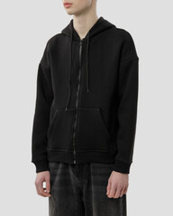 Three-quarters side view of a young man wearing a black zipped hoodie, standing in a studio against a white background. © Vitalii