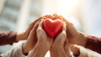A group of people holding a red heart. The heart is surrounded by the hands of the people, and the image conveys a sense of unity and love