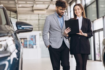 Multi ethnic man and saleswoman discussing car purchase