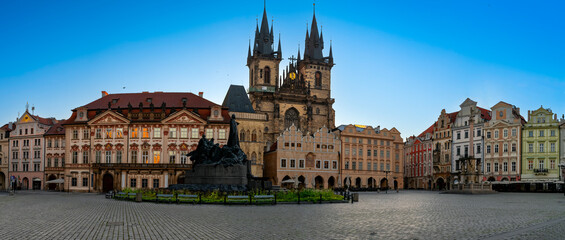 Panoramic view of Prague&rsquo;s Old Town Square with Gothic T&yacute;n Church, Jan Hus Memorial, and historic architecture under a clear blue sky on an early summer morning day.