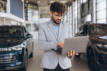Arab businessman using laptop in car dealership