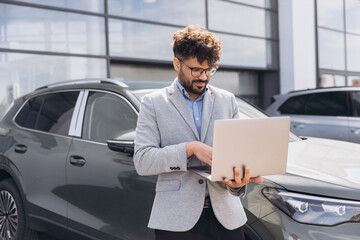 Arab businessman using laptop in car dealership