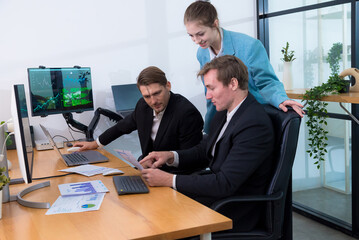 Efficient teamwork modern office setting showcases two men and woman collaborating business analytics. They analyze data laptops, surrounded by greenery, reflecting professional atmosphere