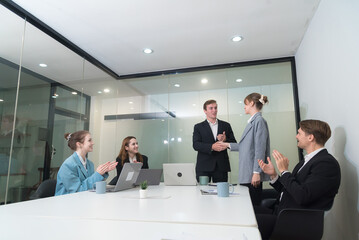 Professional meeting takes place in modern office setting, where man and woman shake hands, symbolizing successful collaboration. Colleagues applaud, showcasing positive and encouraging atmosphere.