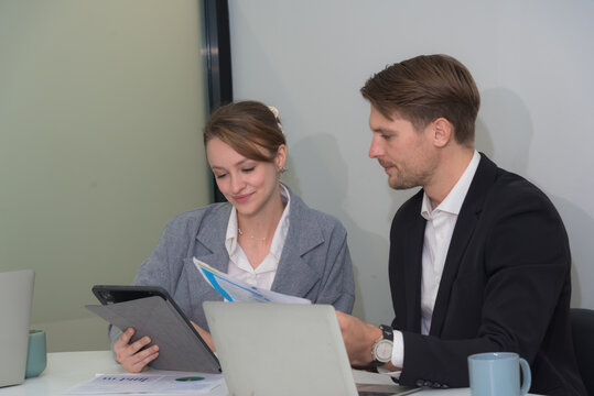 Professional colleagues discussing project documents in modern office setting. woman is reviewing tablet while man is presenting printed materials. Their expressions convey collaboration and focus
