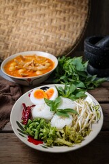 Kanomjeen namya krati ,Rice vermicelli with minced fishes ,Chicken feet,meatballs and coconut milk in red curry on ceramic plate side dish with vegetables and boiled egg