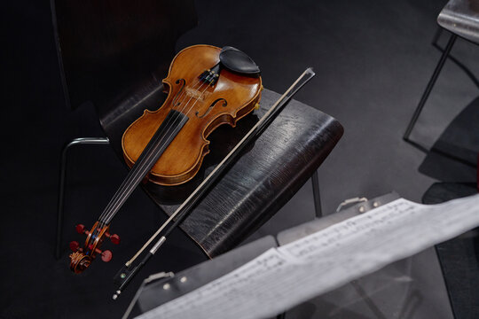 Violin resting on chair with bow placed beside instrument, music sheet visible in foreground, capturing classical music performance preparation scene in concert setting