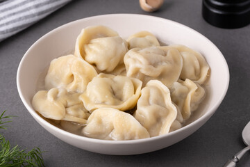A bowl of dumplings sits on a grey countertop, accompanied by fresh herbs and garlic