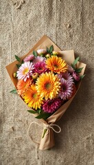 A Vibrant Bouquet of Dahlias in Brown Paper with Twine Tie on Woven Fabric Background