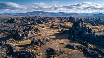 Aerial view of lava field landscape with jagged rock formations and distant mountains under a cloudy sky