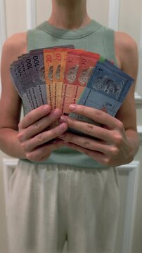 Close-up of woman holding Malaysian Ringgit MYR banknotes indoors. Concept of finance, money management, salary, payment, savings, investment, business and economy in Malaysia.