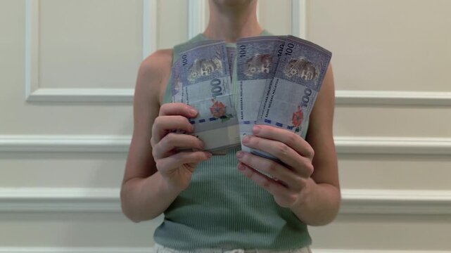Close-up of woman counting Malaysian Ringgit MYR banknotes indoors. Concept of finance, money management, salary, payment, savings, investment, business and economy in Malaysia.