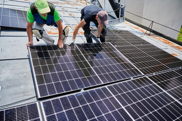 Workers building solar panel system on metal rooftop of house. Two men installers installing photovoltaic solar module outdoors. Alternative, green and renewable energy generation concept.