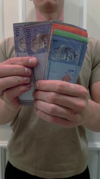 Close-up of man counting Malaysian Ringgit MYR banknotes indoors. Concept of finance, money management, salary, payment, savings, investment, business and economy in Malaysia.