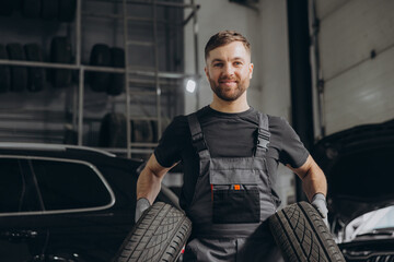 Auto mechanic holding car tires at garage