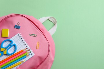 Colorful school supplies arranged around a backpack on a pastel green background. Back to school concept