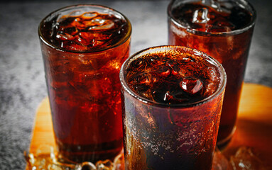 Cola soft drink with ice cubes, soda fizzy drink in Cold three glass on gray background, close-up