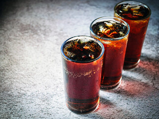 Cola soft drink with ice cubes, soda fizzy drink in Cold three glass on gray background, close-up