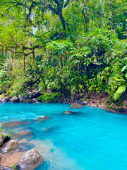 Turquoise waters of Rio Celeste flowing between rocks and dense green rainforest vegetation in Costa Rica.