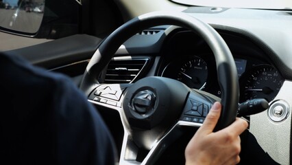 Male arms holds steering wheel while driving a motor car at city. Young man operating the automobile at urban road. Driver moving in his auto on route. Slow motion