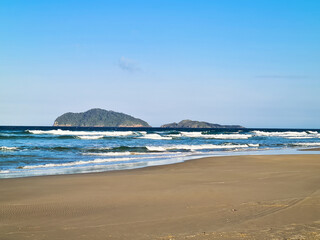 View of Spider Island observed from Santinho Beach in Florianópolis, Santa Catarina, Atlantic Ocean on a sunny day with a blue sky.