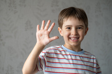 Emotional portrait of caucasian smiling little boy wearing striped t-shirt, stretching his right hand up for greeting. Happy child waving hand, say Hi