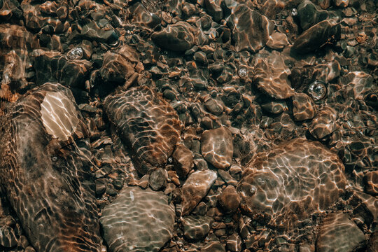 A detailed view of sunlight shimmering on a clear water riverbed highlighting smooth stones and rocks.