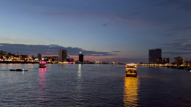 Phnom Penh riverside in Cambodia at dusk, with illuminated boats cruise along the river. Vibrant nightlife scene highlights the charm of Cambodia&rsquo;s capital, blending modern city energy with relax flow
