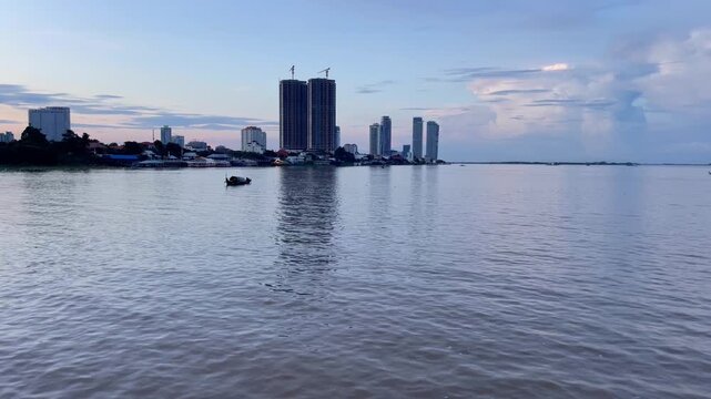 Peaceful evening view of Phnom Penh, Cambodia, showing the wide river with calm water and the skyline in the background. Coexistence of traditional river life and modern growth concept