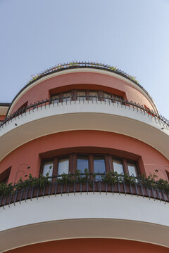 View of a unique building with a curved facade, painted in vibrant coral and accented by crisp white bands, stands tall against a clear blue sky, L'Aquila, Abruzzo, Italy.