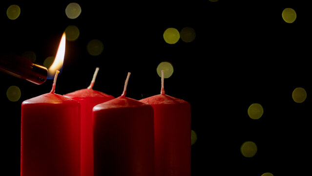 Hand lighting first red candle in the Advent wreath on a festive background with golden decorations, close up shot. Holiday and tradition concepts.