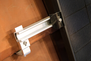 Close-up of solar panel mounting system with metal rail and clamp fixed on roof tile, showing...