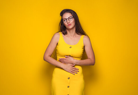 Stomach ache, woman suffering from stomachache, isolated on yellow background. Ill girl with chronic gastritis. Abdomen bloating concept.
