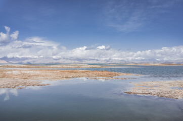 Panorama landscape of Lake Karakul in the Pamir mountains in the Tien Shan against the background of high snowy rocky peaks with clouds, morning panorama of the lake for the background