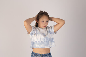 Young girl is posing with her hands behind her head,looking slightly downwards..