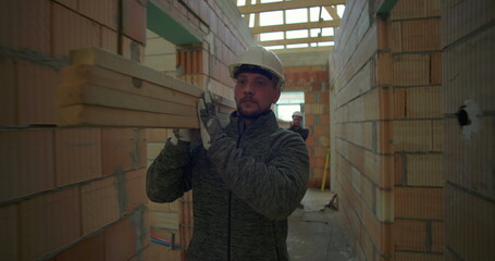 Construction worker carrying planks through corridor in house under construction, displaying focus...
