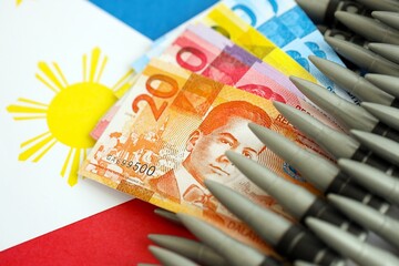Philippines peso currency money bills and rifle bullets on flag. The concept of warfare and gun...