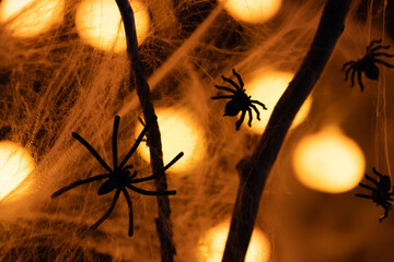 Spooky plastic spiders and fake cobwebs draped on dark branches, illuminated by glowing orange bokeh lights, perfect Halloween decoration