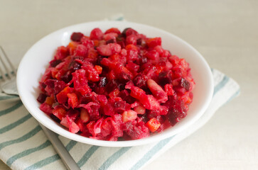 Salad vinaigrette in a white bowl with a fork on a striped napkin on a gray table. Concept of vegan and vegetarian cuisine. Horizontal orientation. Selective focus.