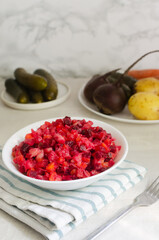 Salad vinaigrette in a white bowl on a gray table. Vegetable salad of boiled beets, potatoes, carrots, pickles, sauerkraut and beans. Vertical orientation. Selective focus.