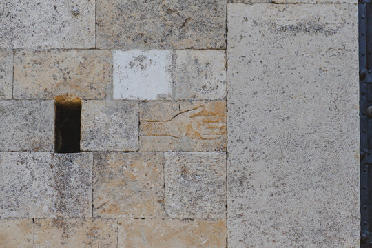 View of hand carving etched into the textured stone wall, a small dark rectangular opening adds depth, creating a striking contrast, Bominaco, Abruzzo, Italy.