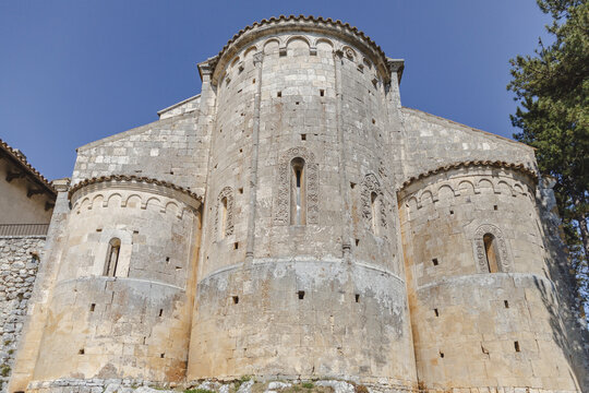 View of the ancient church rises with weathered stone and rounded apses against a clear sky in Bominaco, Abruzzo, Italy.