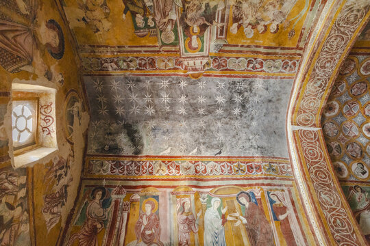 View of ancient frescoes adorn the interior walls and ceiling, a celestial scene twinkling above figures in rich, earthy hues, Bominaco, Abruzzo, Italy.